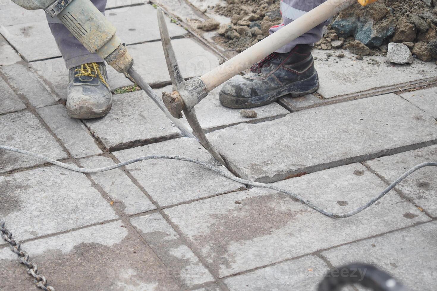 A construction worker is currently using an electric jackhammer to break up pavement tiles photo