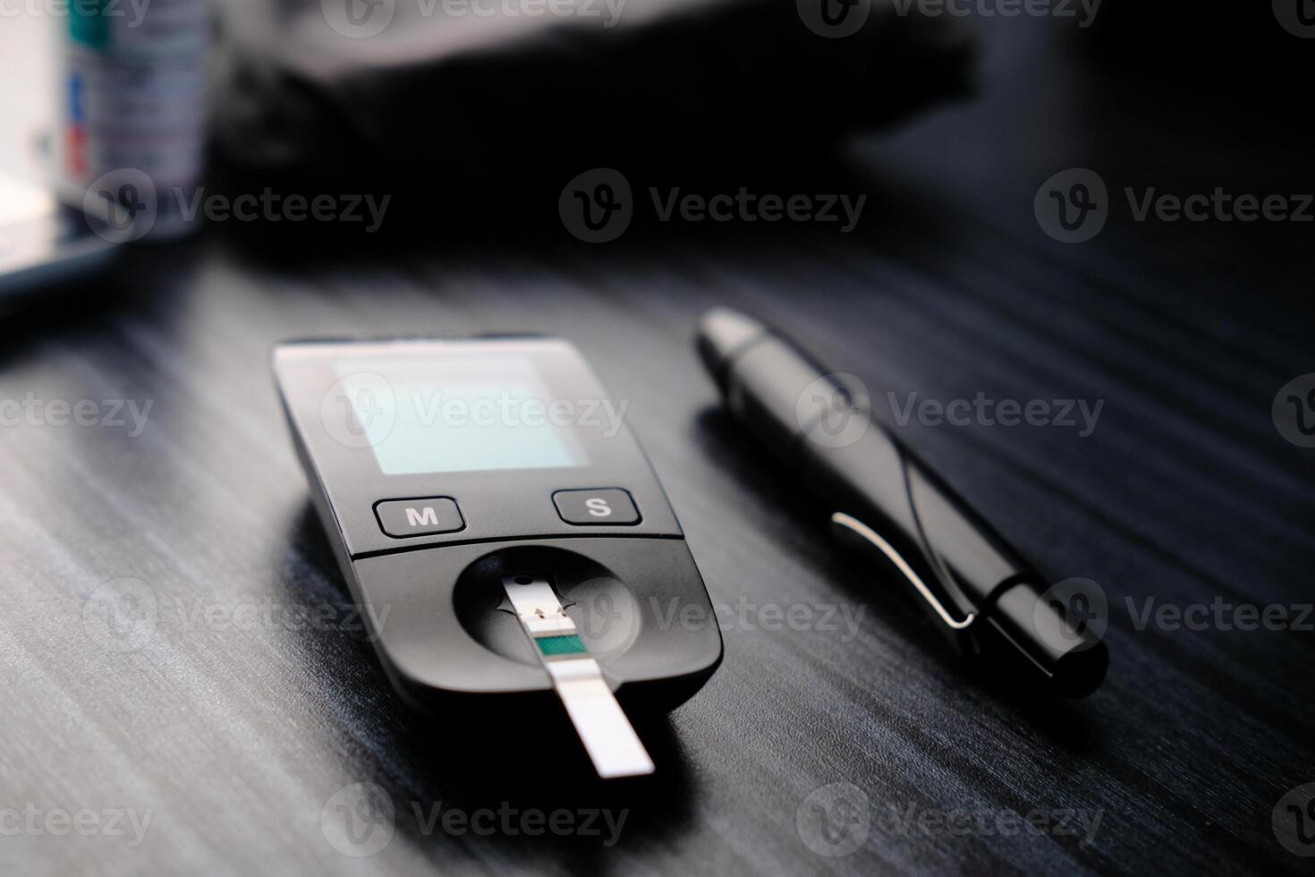Here is a Diabetes Monitoring Device featuring a Test Strip and Pen placed on the Table photo