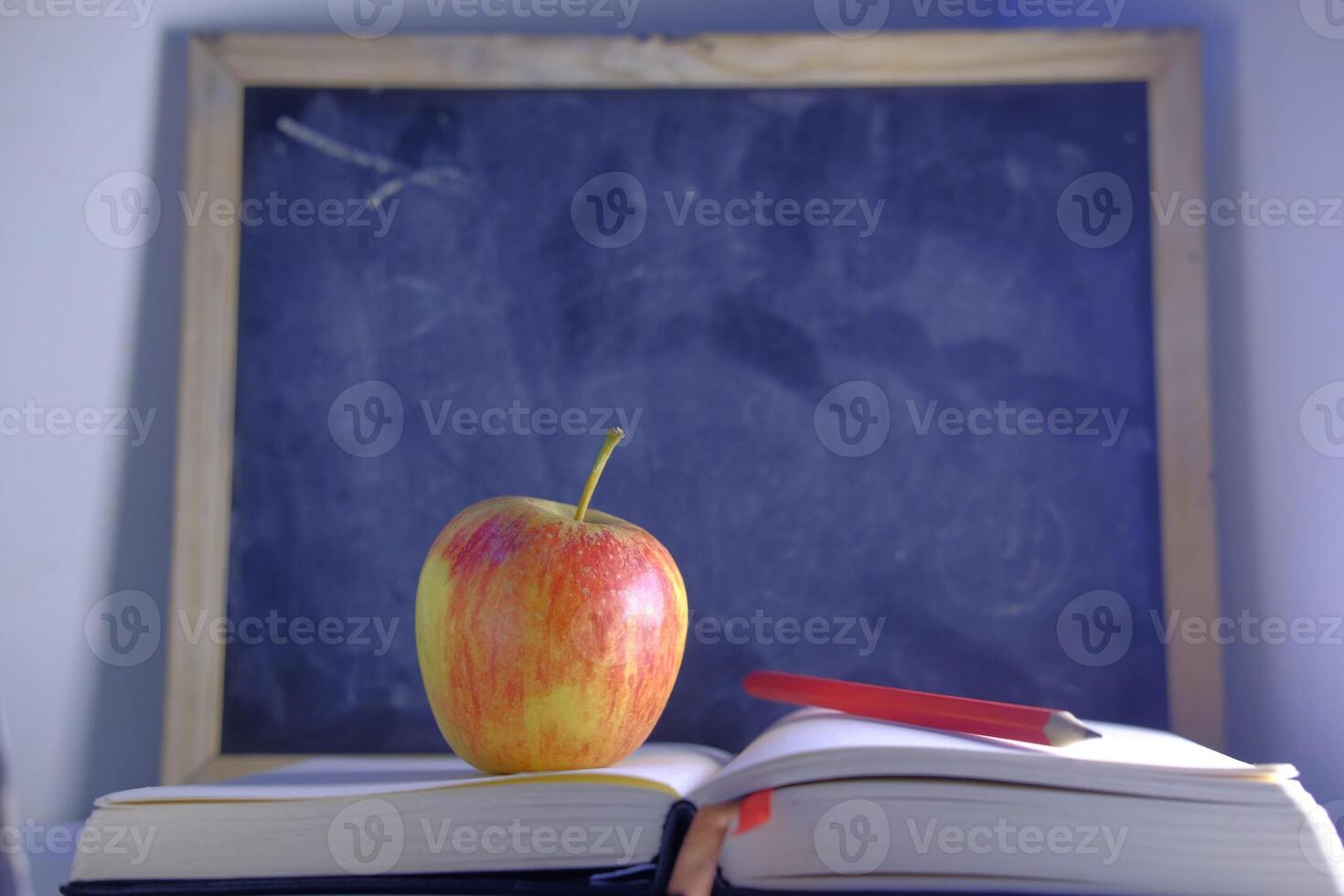 An image features an apple placed on books with a blackboard background in an educational setting photo