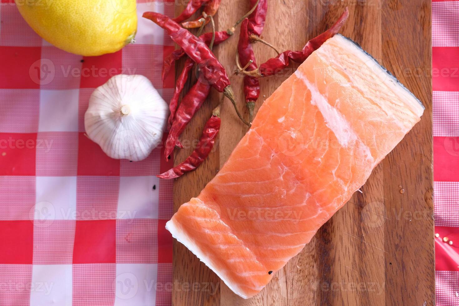 Fresh Salmon Fillet with Garlic, Lemon, and Chili Peppers on a Rustic Wooden Board photo