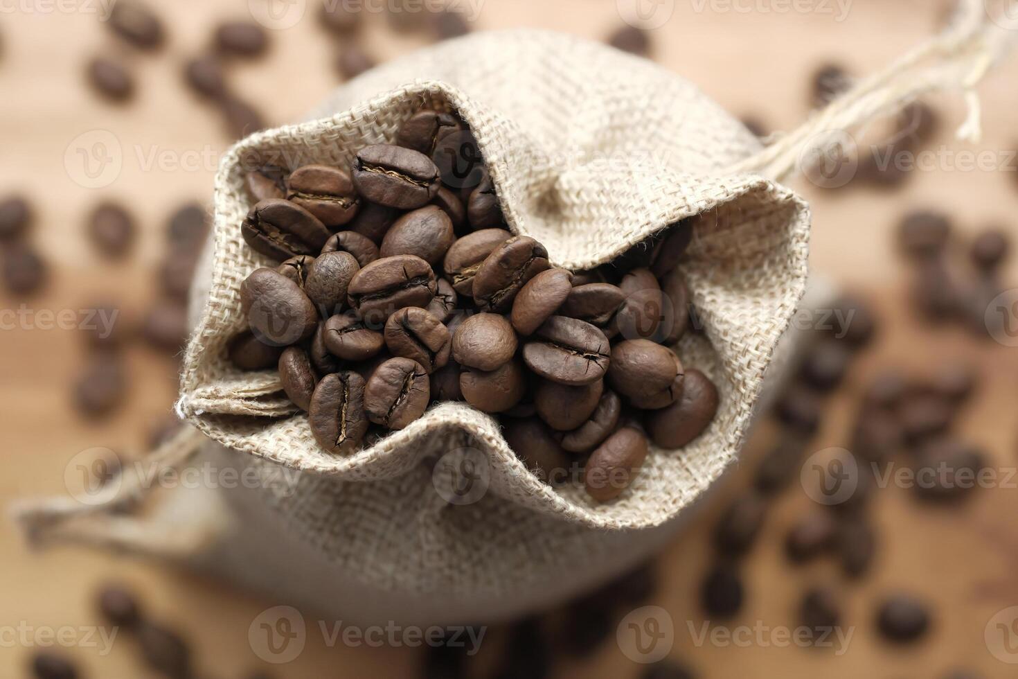 A burlap sack filled with freshly roasted coffee beans placed on a rustic wooden table photo