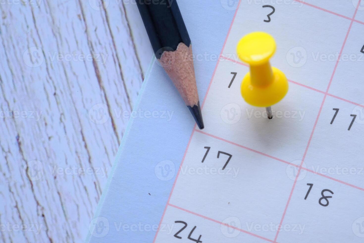 A CloseUp Image of a Calendar Featuring a Pencil and a Bright Yellow Push Pin on a Wooden Table photo