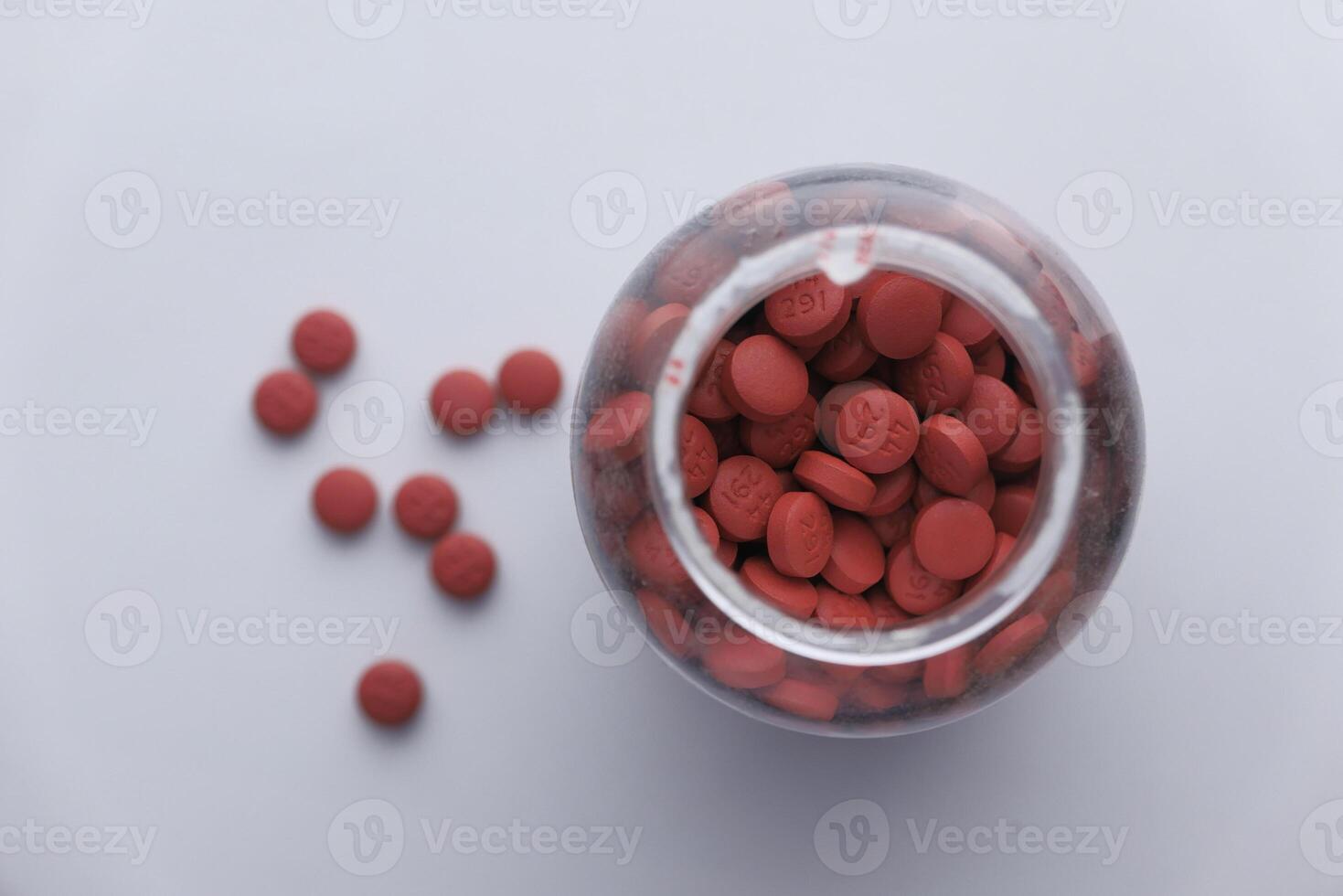 Bright Red Round Tablets Stored in a Transparent Glass Jar on a Crisp White Background photo
