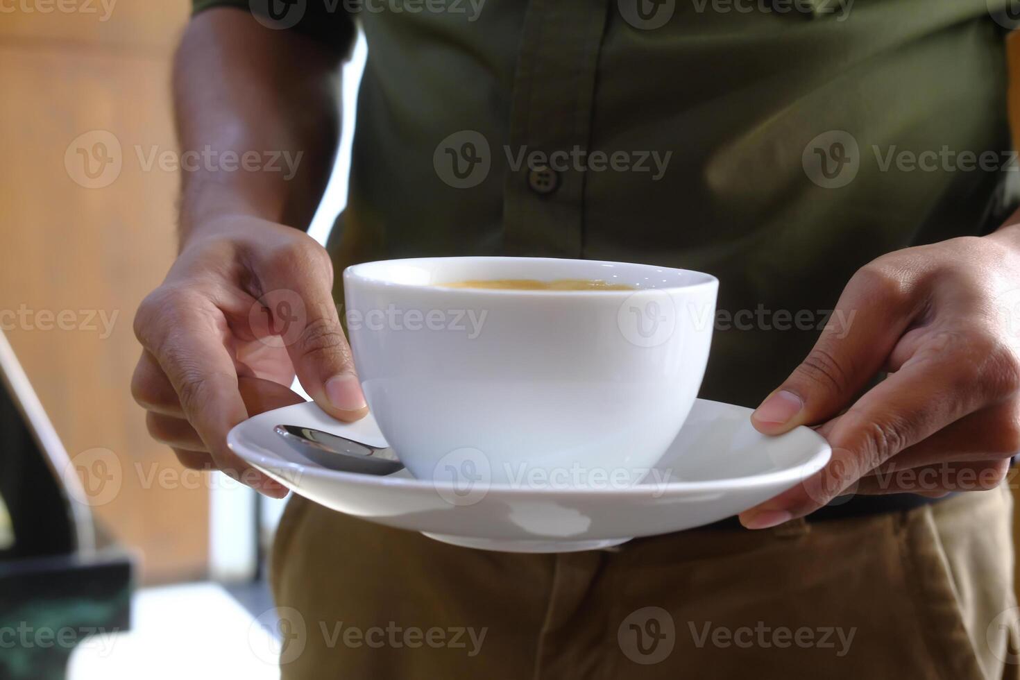 Two hands holding a white ceramic cup of coffee on a matching saucer in a cozy cafe photo