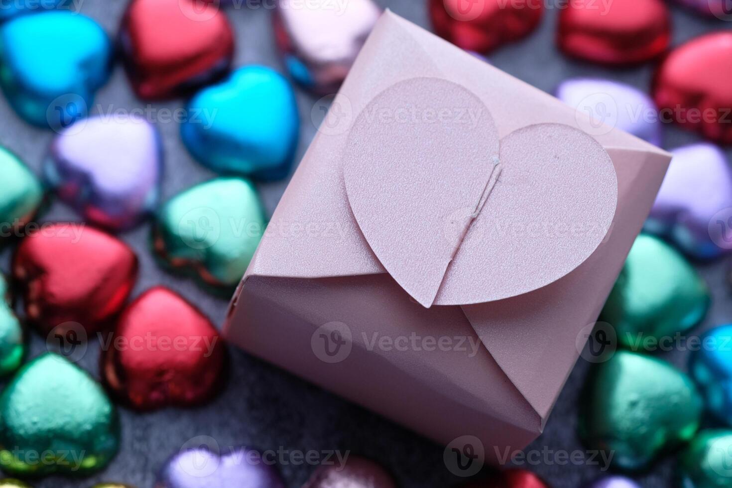 A Beautifully Wrapped Gift Box Surrounded by a Variety of Colorful Heartshaped Chocolates photo