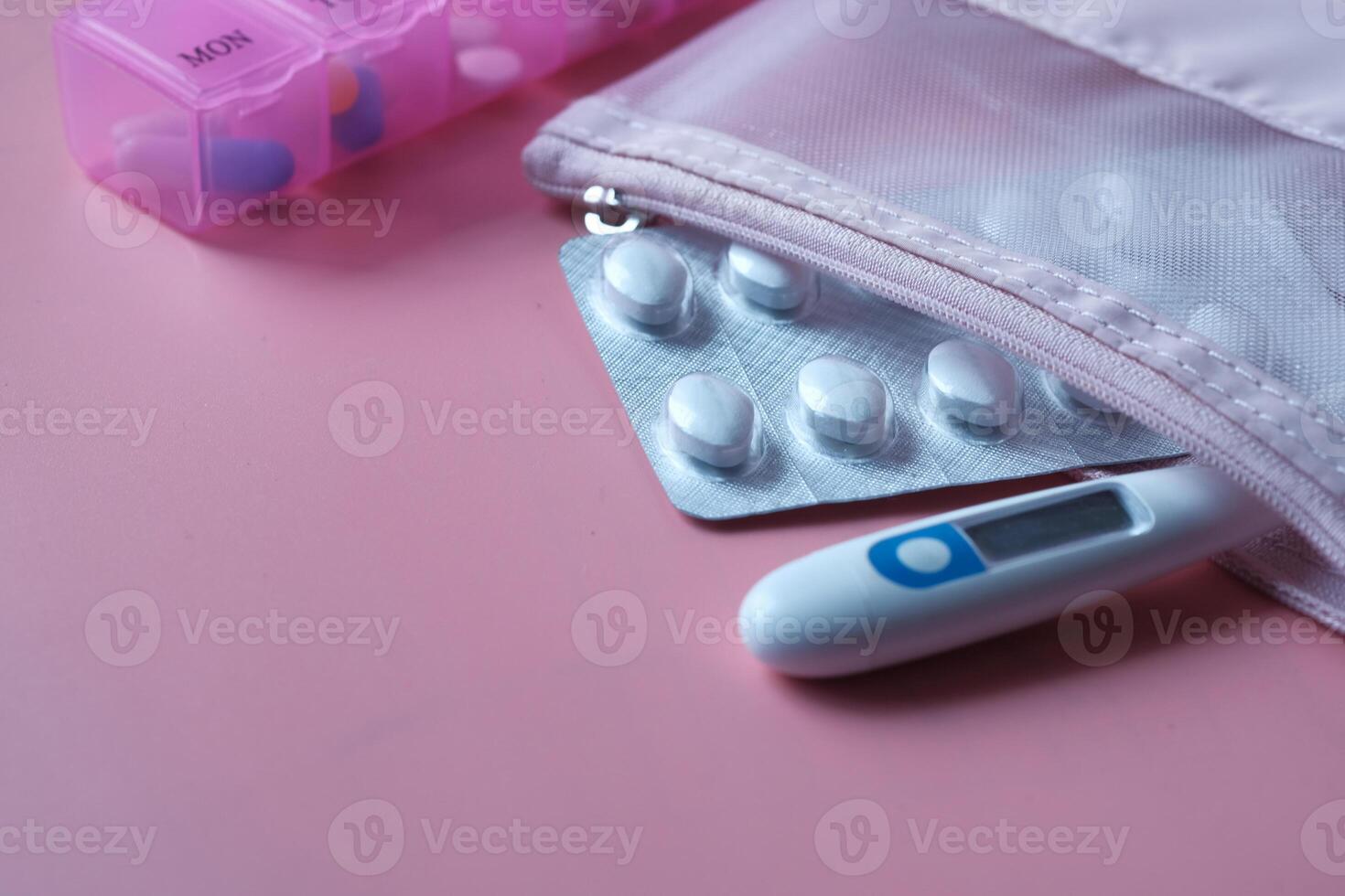 Medical Essentials A Thermometer, Various Pills, and a Pill Organizer on a Pink Background photo