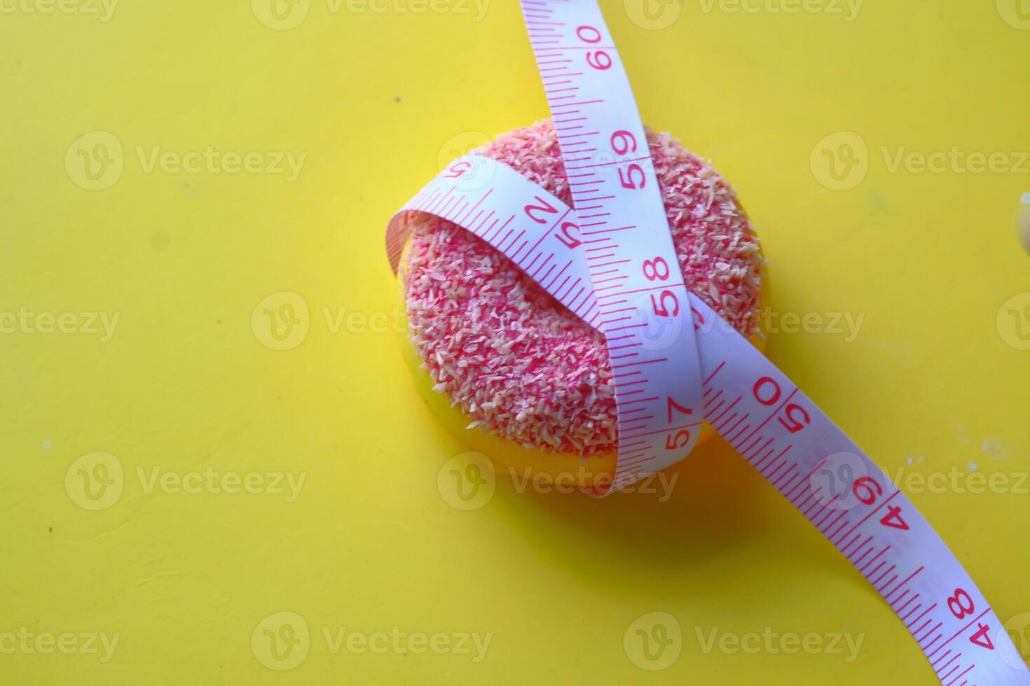 Measuring a bright pink donut using a tape measure against a vibrant yellow background photo