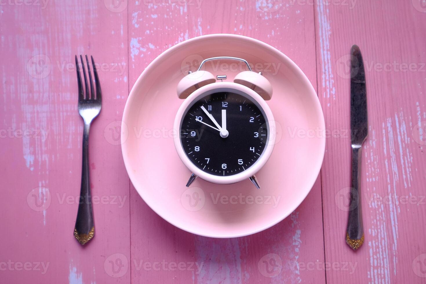 An Alarm Clock is beautifully placed on a Pink Plate accompanied by Cutlery Its Time for Breakfast photo