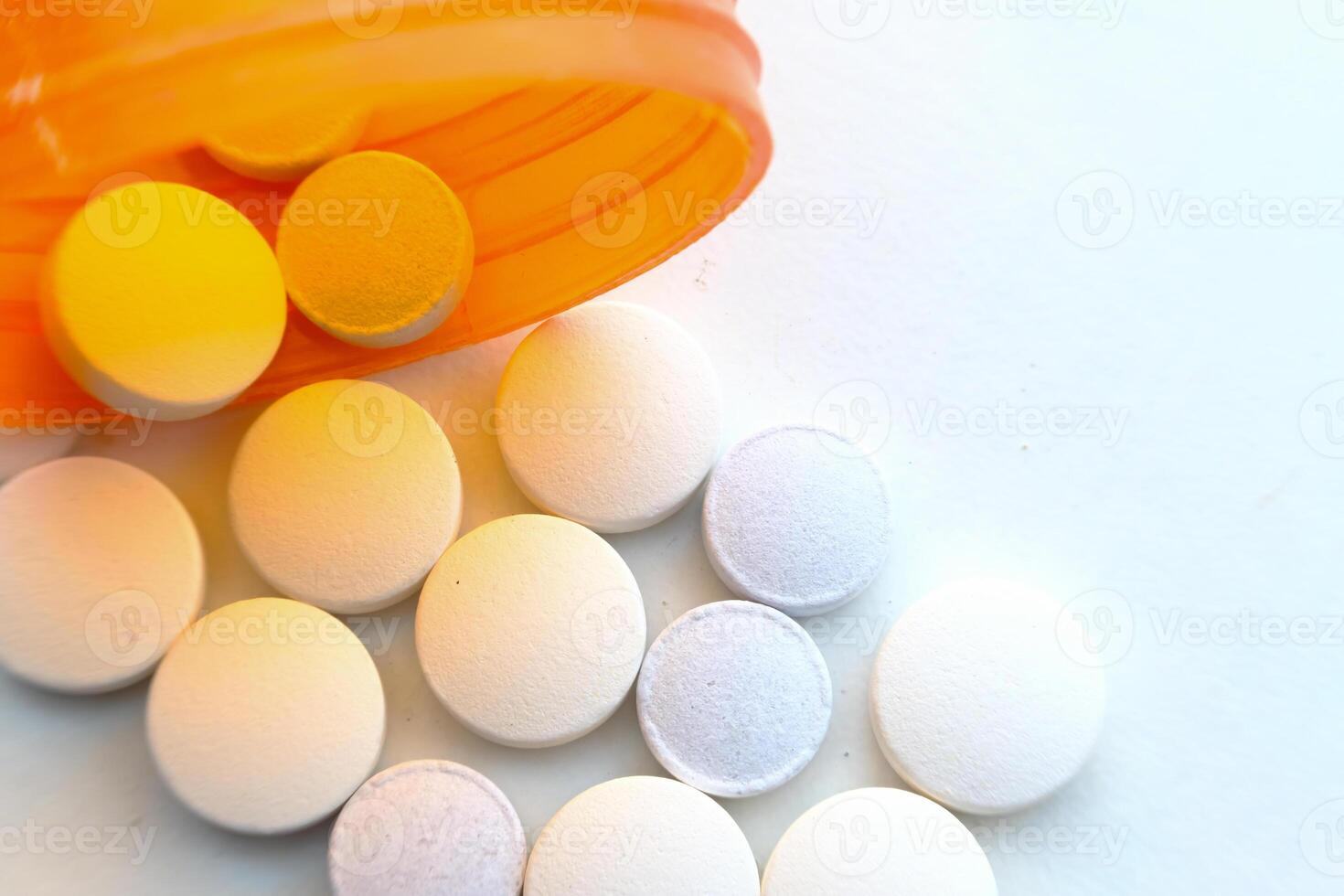 A variety of assorted pills were spilled out from a prescription bottle onto the surface photo