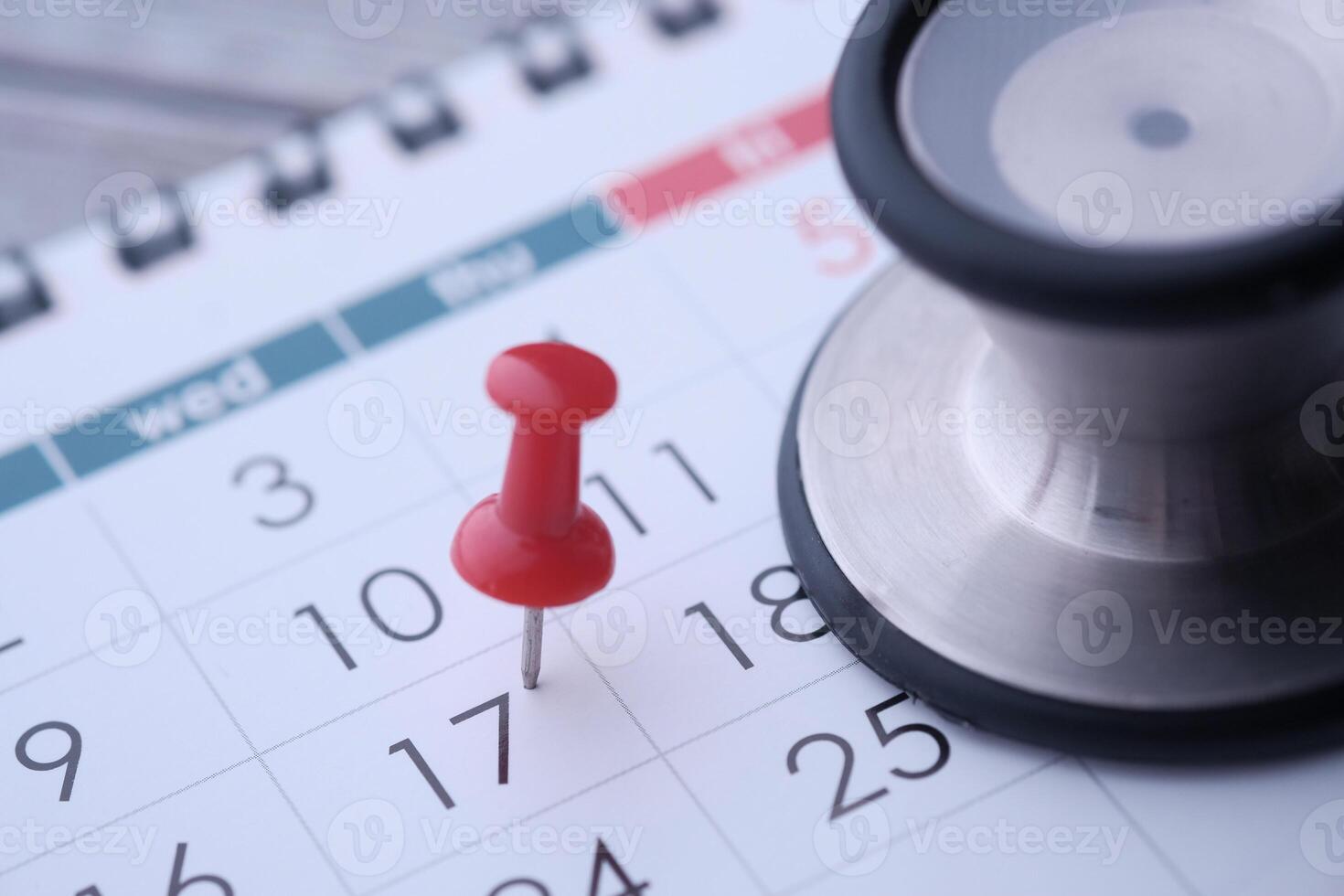 A stethoscope and a red thumbtack placed on a calendar signify health appointments and schedules photo