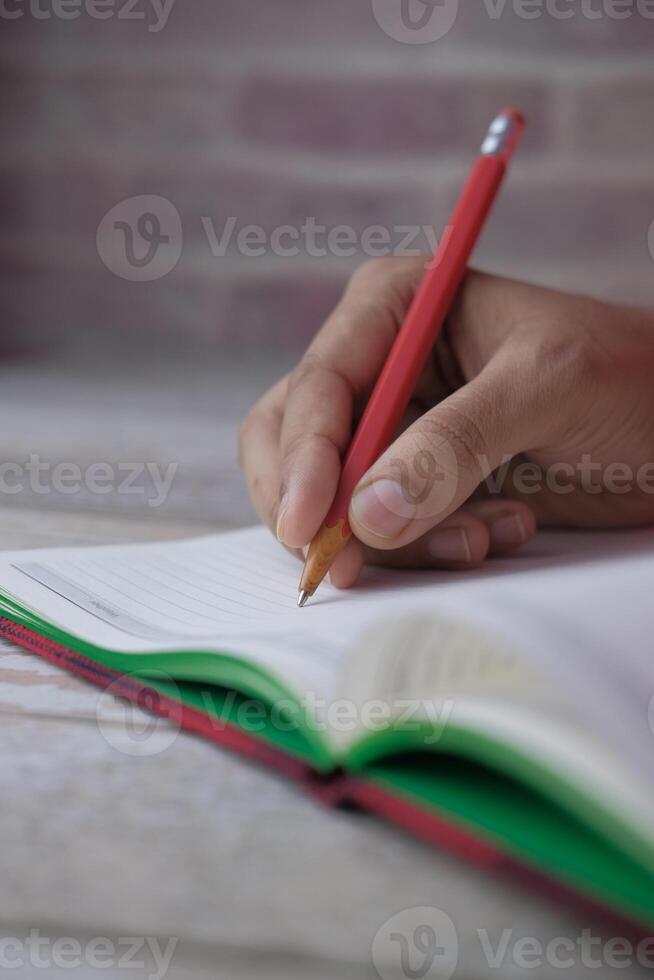 A Person Engaged in Writing in Their Notebook While Using a Red Pencil to Create Ideas photo