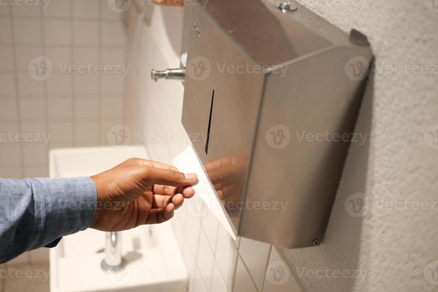 Hand Using Paper Towel Dispenser in a Hygienic Public Restroom with Clean White Tiles photo