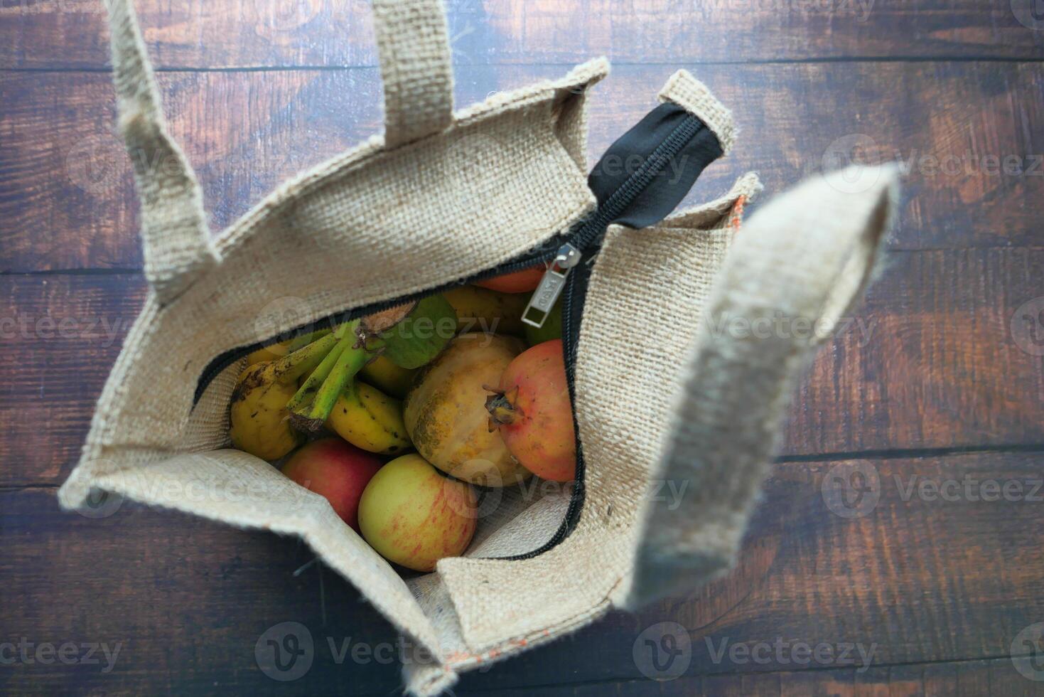 An overhead view of a tote bag filled with fresh fruits on a wooden table surface photo