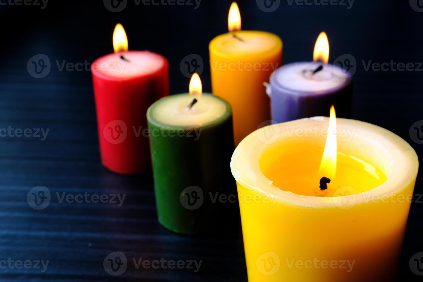 A display of vibrant, colorful candles with flickering flames against a dark background photo