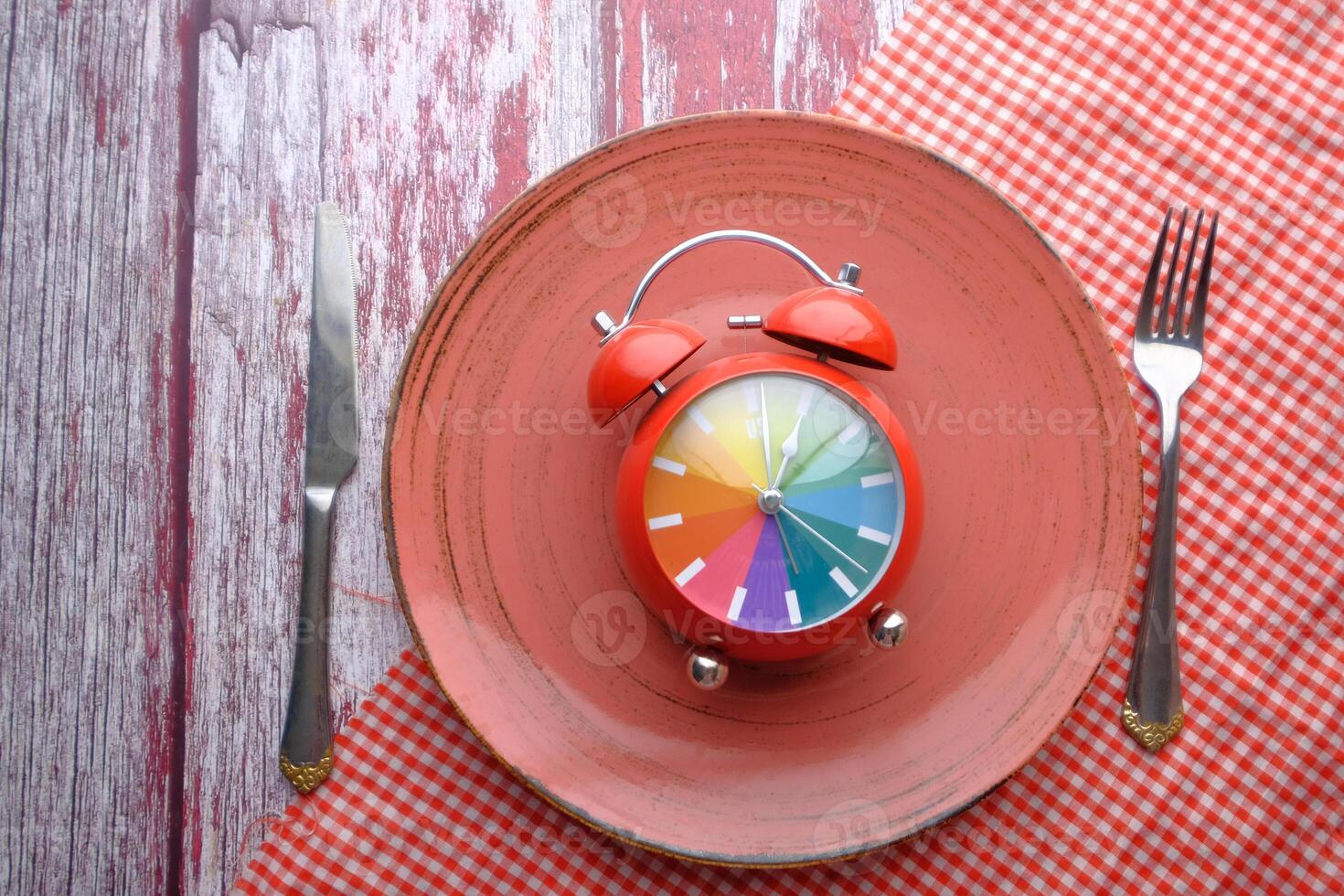 A vibrant and colorful alarm clock beautifully placed on a plate accompanied by cutlery photo