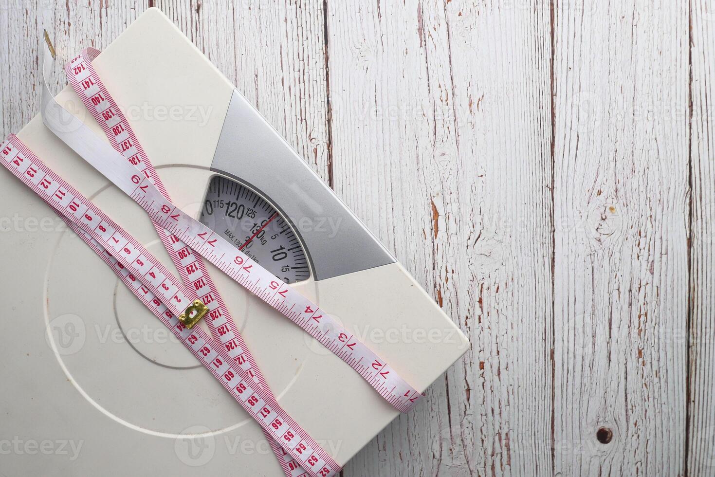 A Bathroom Scale paired with a Measuring Tape, both positioned gracefully on a Wooden Background photo