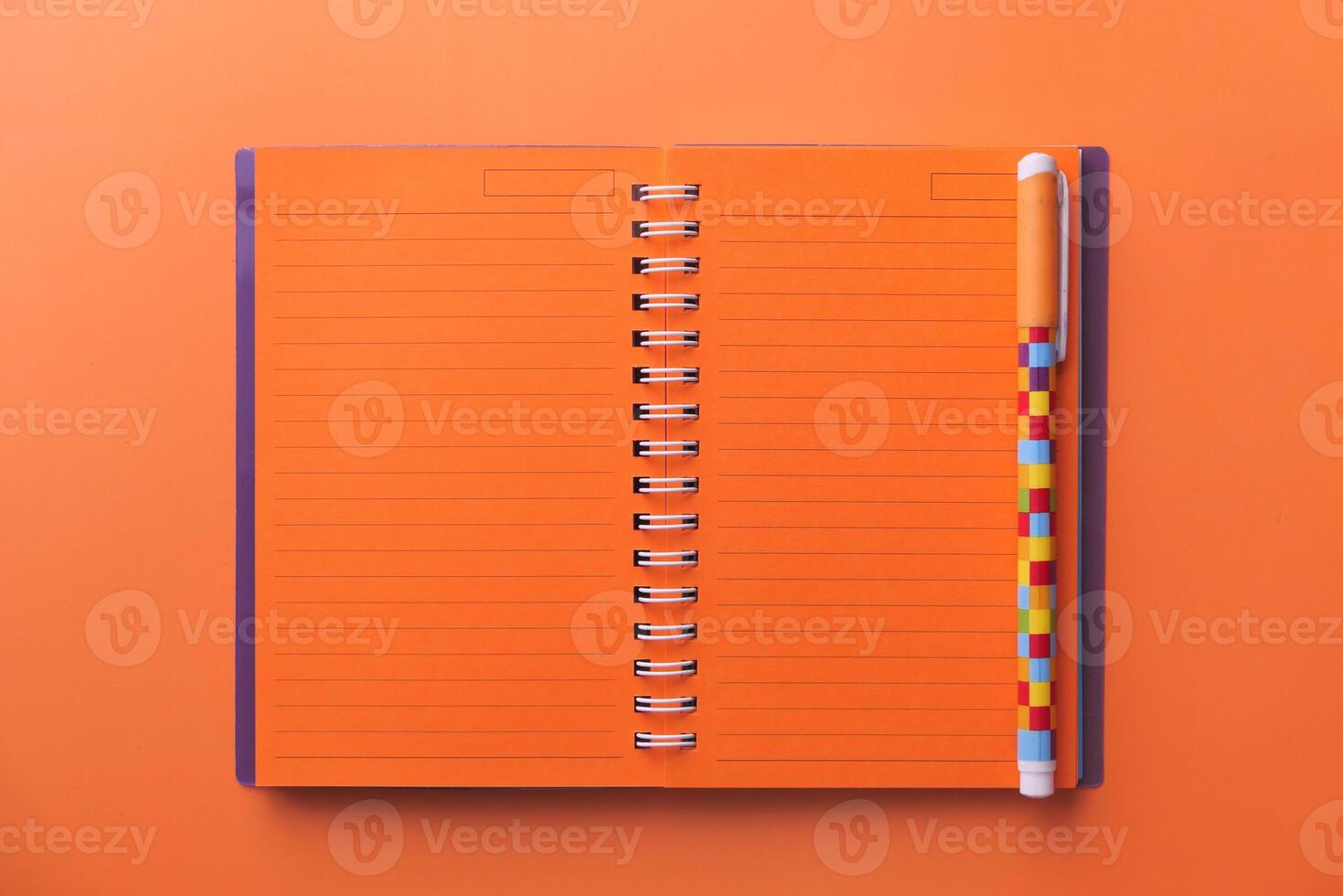 A Vibrant Orange Notebook is Open with a Colorful Pen Laying on a Light Background Surface photo