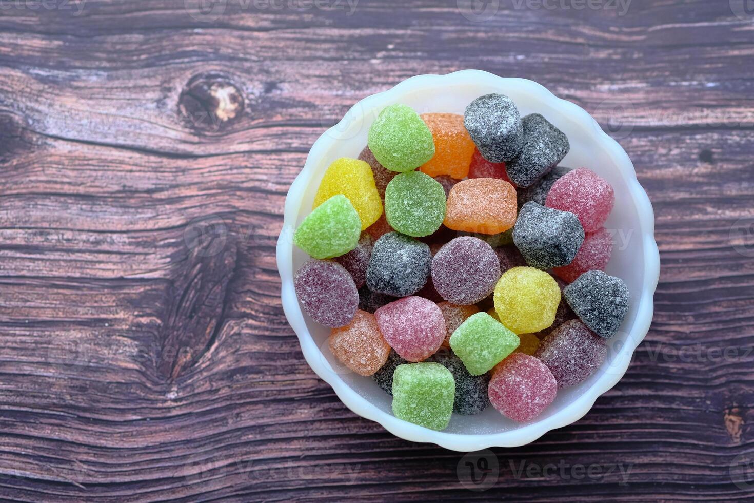 A Vibrant and Colorful Assorted Candy Displayed in a White Bowl on a Rustic Wooden Background photo