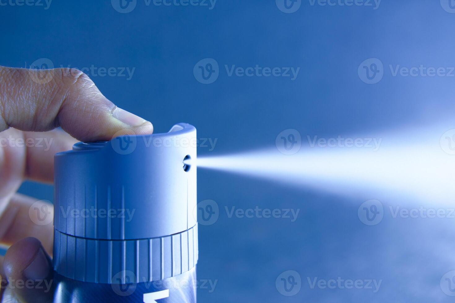 Closeup image depicting a hand actively pressing a spray can, releasing a fine mist of liquid photo