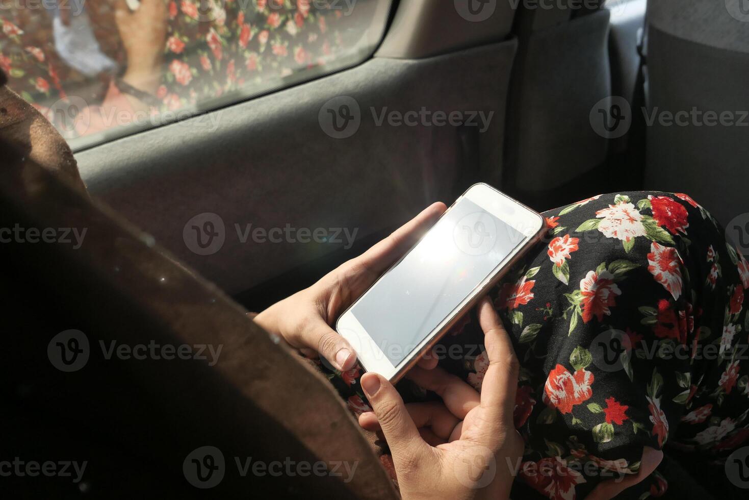 A person wearing a vibrant floral dress is using a smartphone while sitting in a car photo