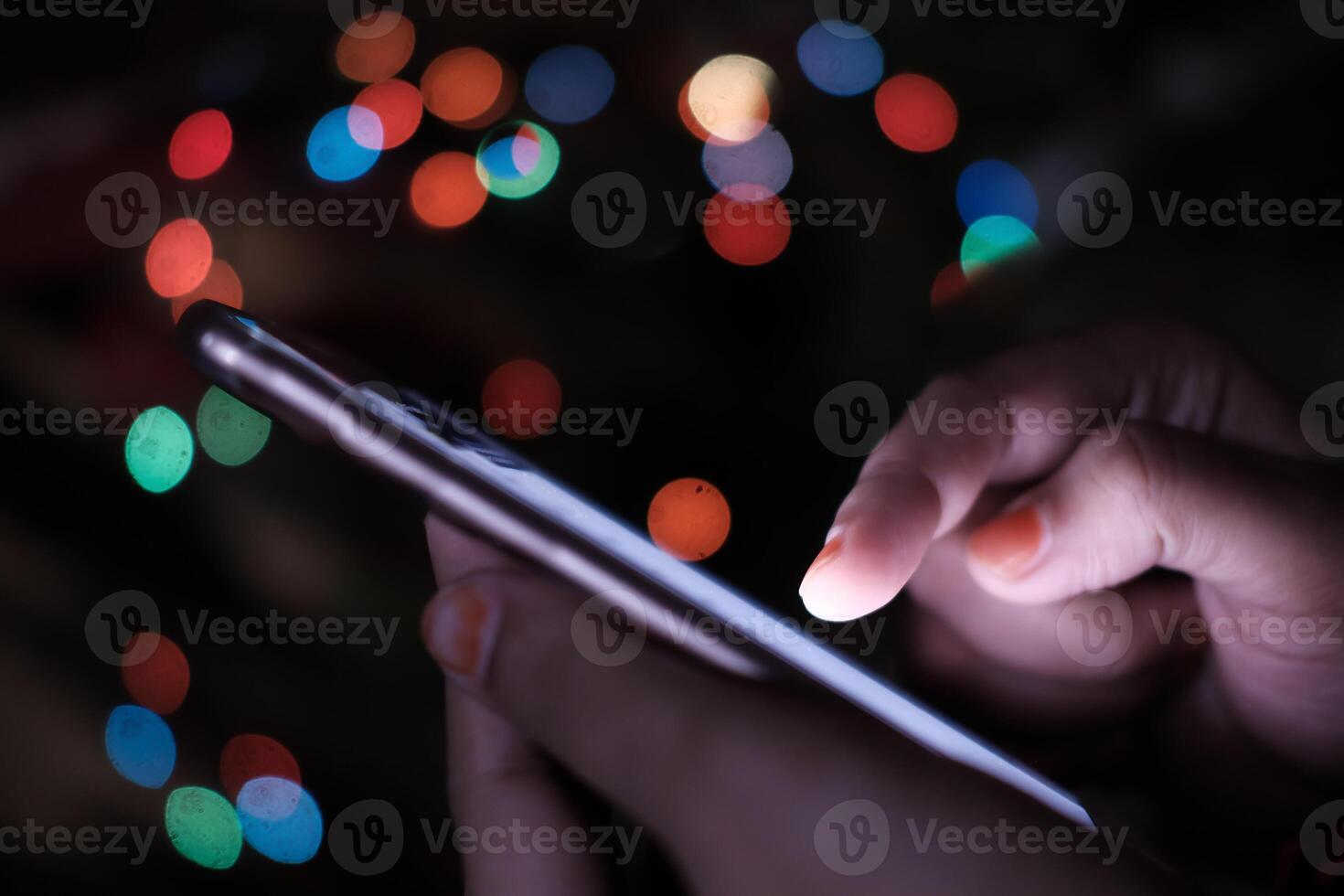 A person attentively using a smartphone surrounded by a vibrant and colorful bokeh background photo