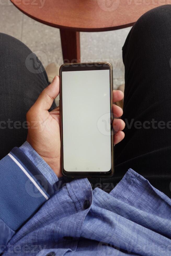 A person is sitting comfortably in a relaxed position, holding a smartphone that has a blank screen photo