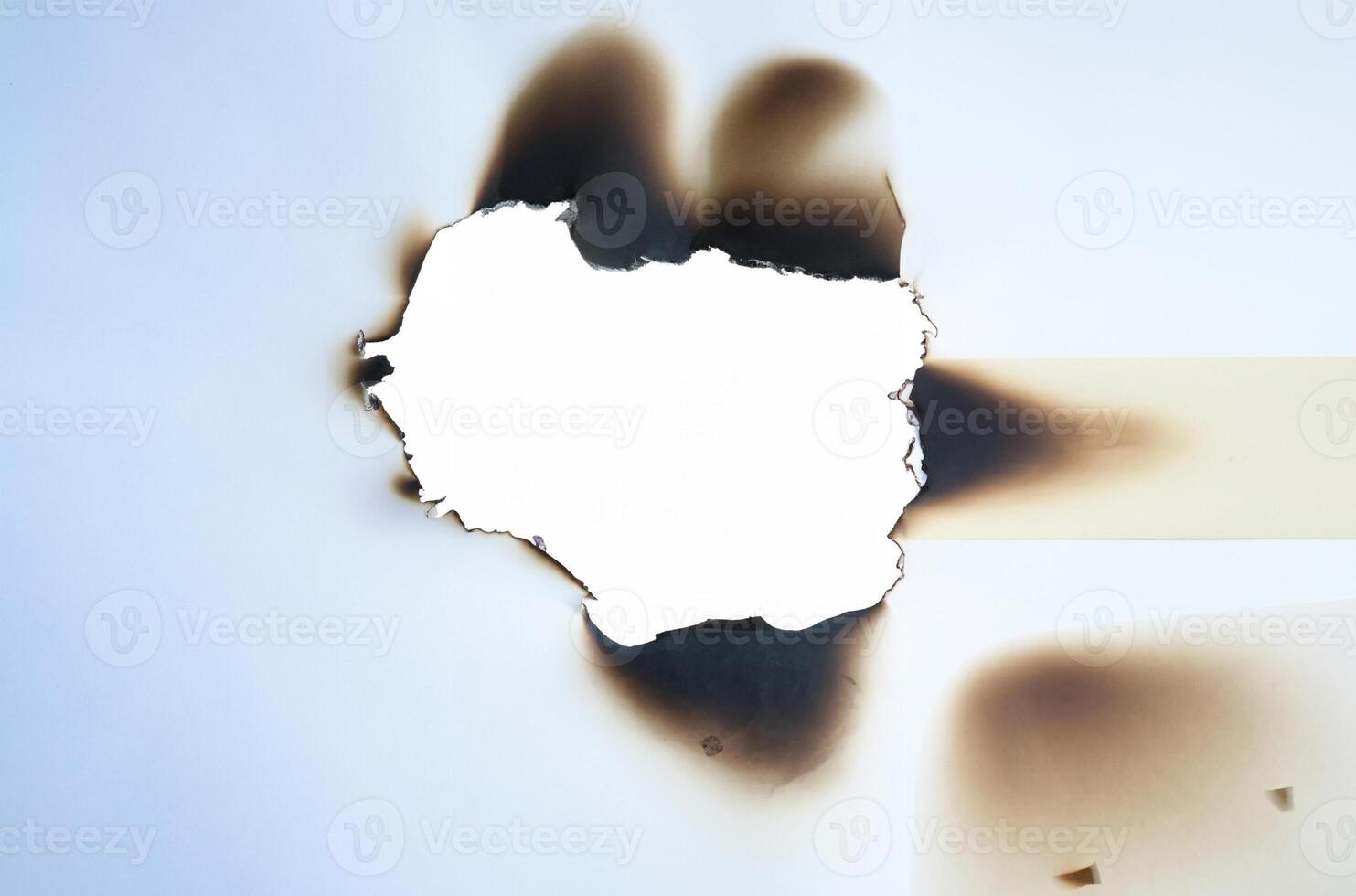 A burnt hole in white paper with irregular scorched edges and slight smoke marks, ideal for use in design projects or as a texture element. photo