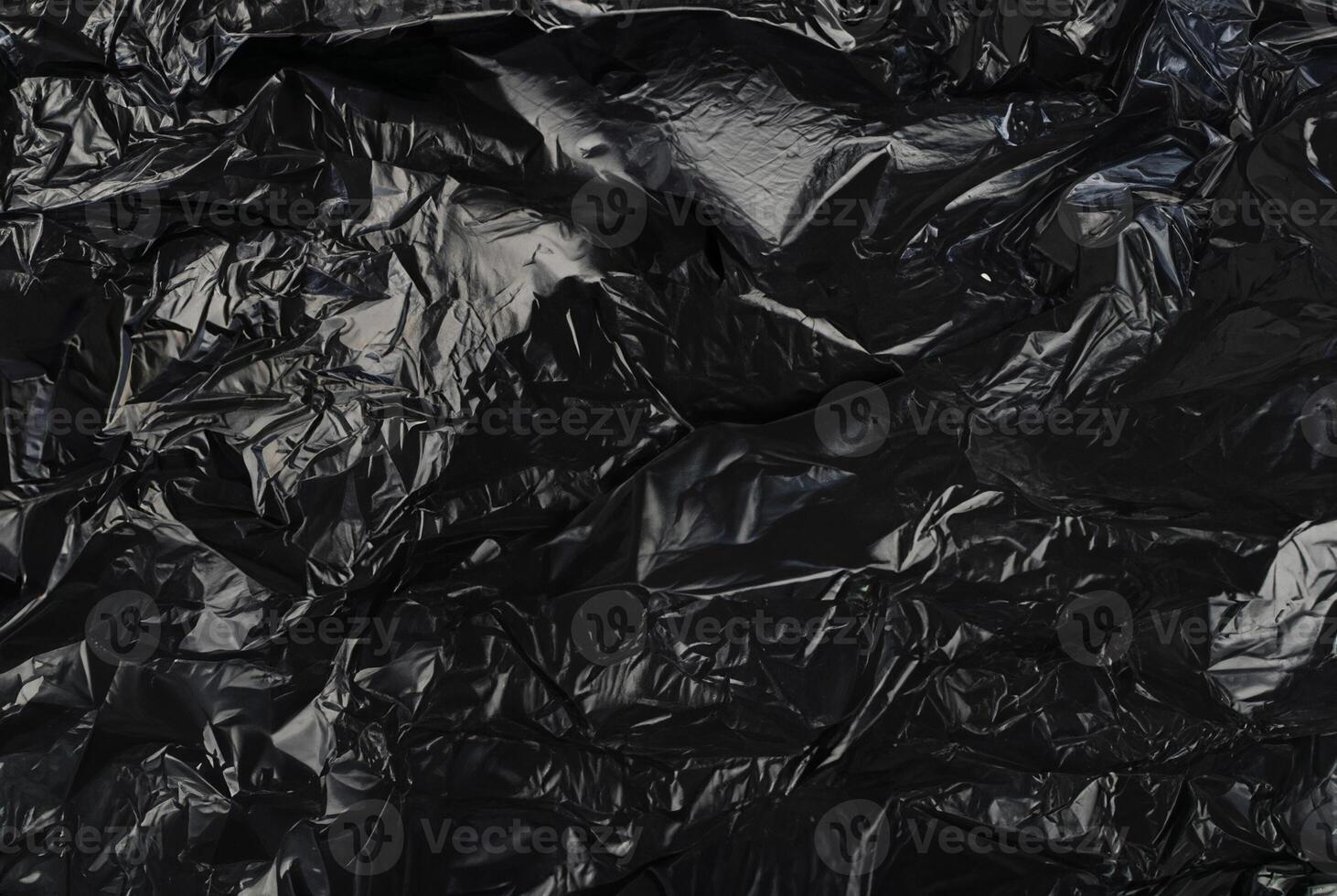 Close-up of a crumpled black plastic material with irregular folds and shiny surface. photo