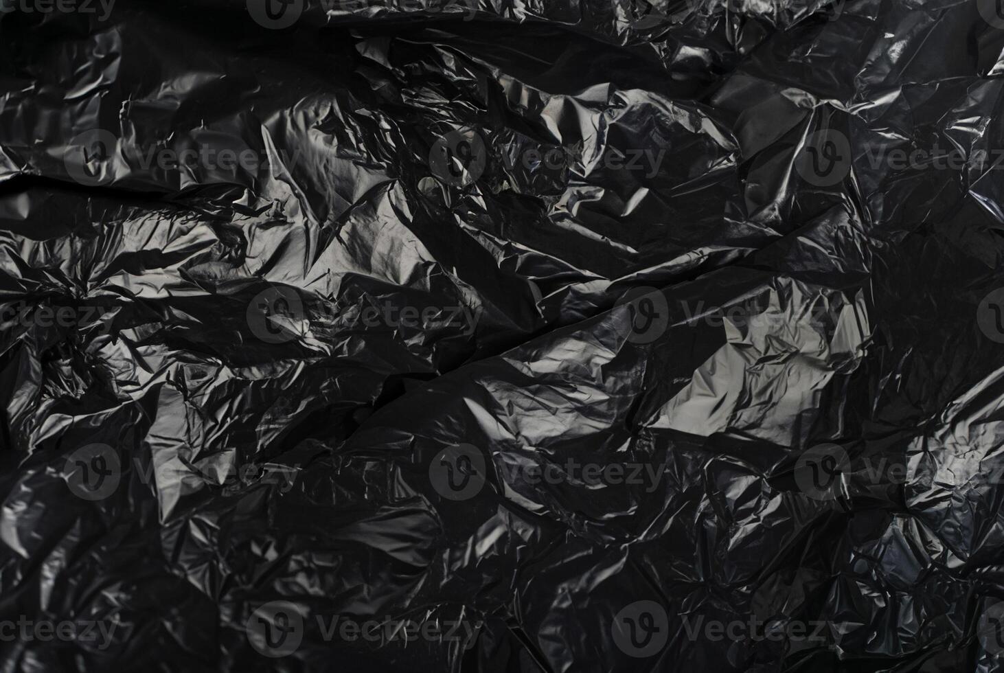 Close-up of a crumpled black plastic material with irregular folds and shiny surface. photo