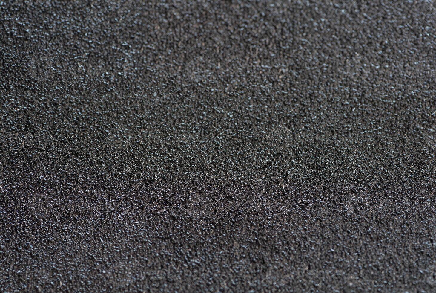 Detailed close-up of a rough black sandpaper texture, ideal for backgrounds, construction, or industrial themes. photo