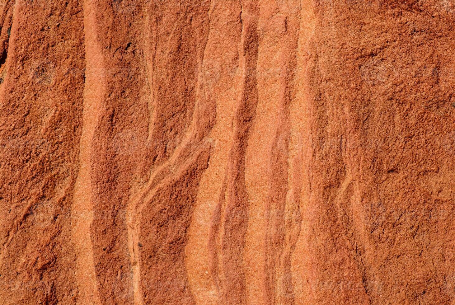 Close-up of red sandstone rock texture featuring natural wavy patterns and rough surface. photo