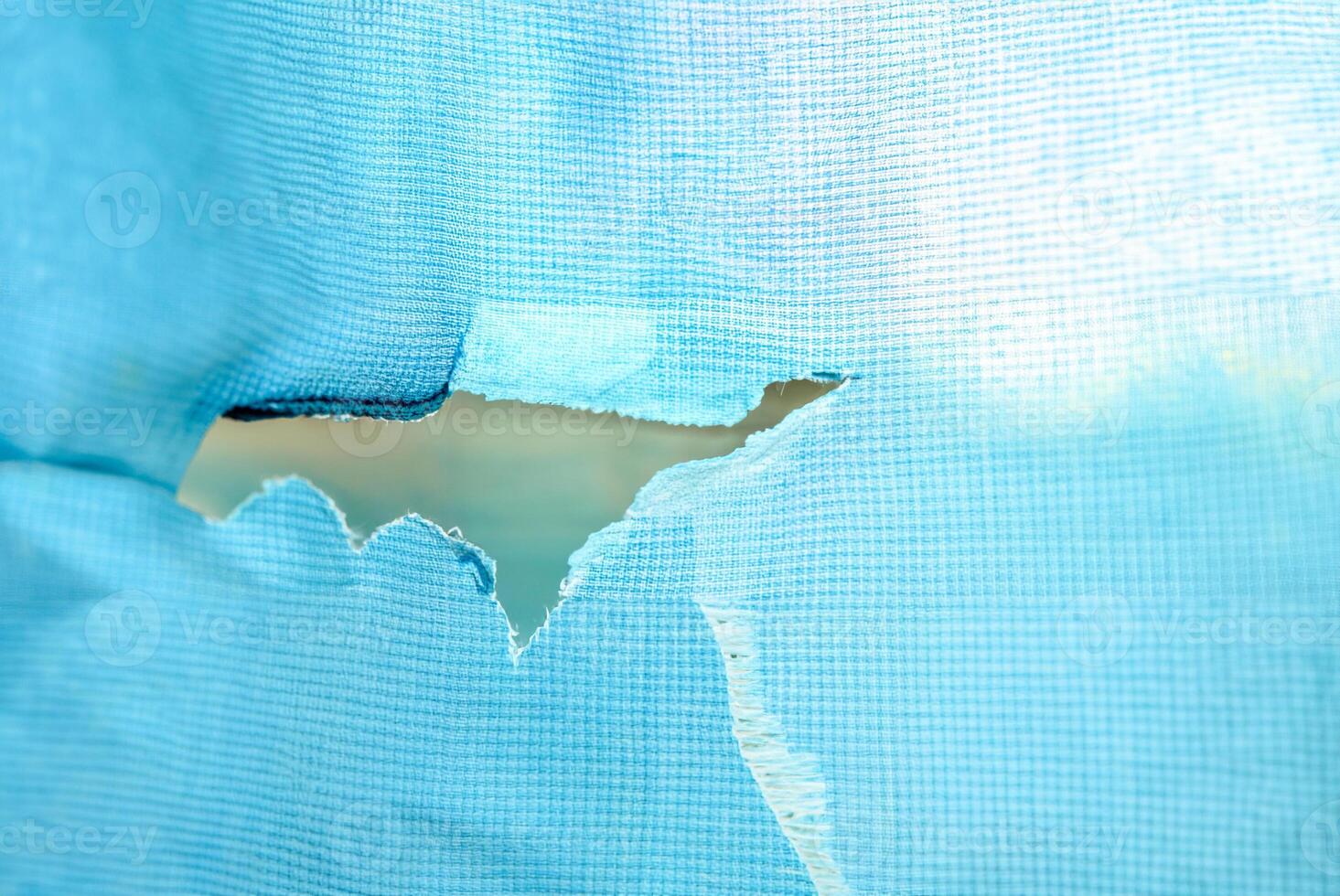 Close-up of a torn blue fabric with a rip in the center, showing visible texture and wear, ideal for concepts of damage or imperfection. photo