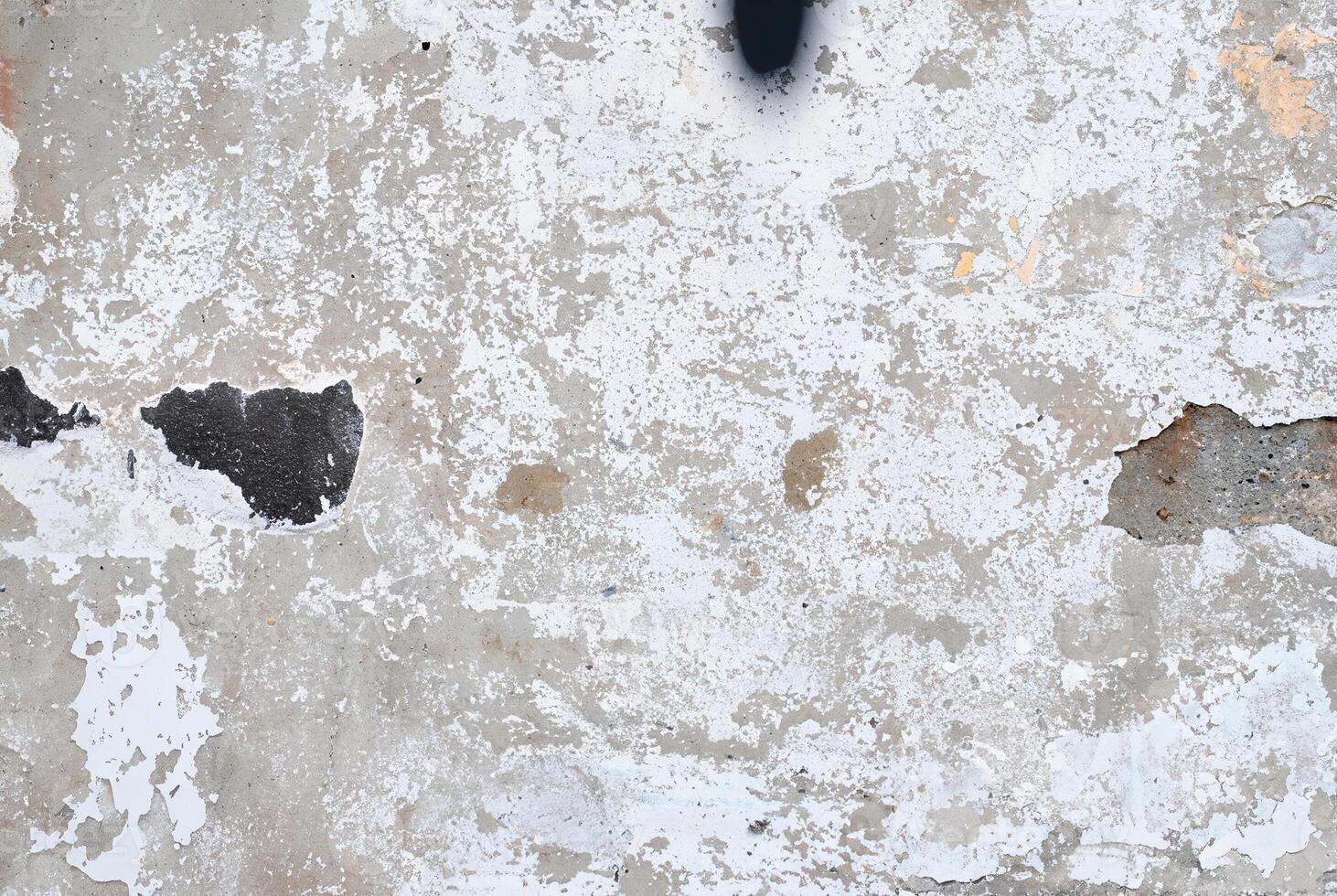 Close-up of a weathered concrete wall with peeling paint and rough textures, ideal for use in grunge designs, backgrounds, and industrial-themed projects. photo