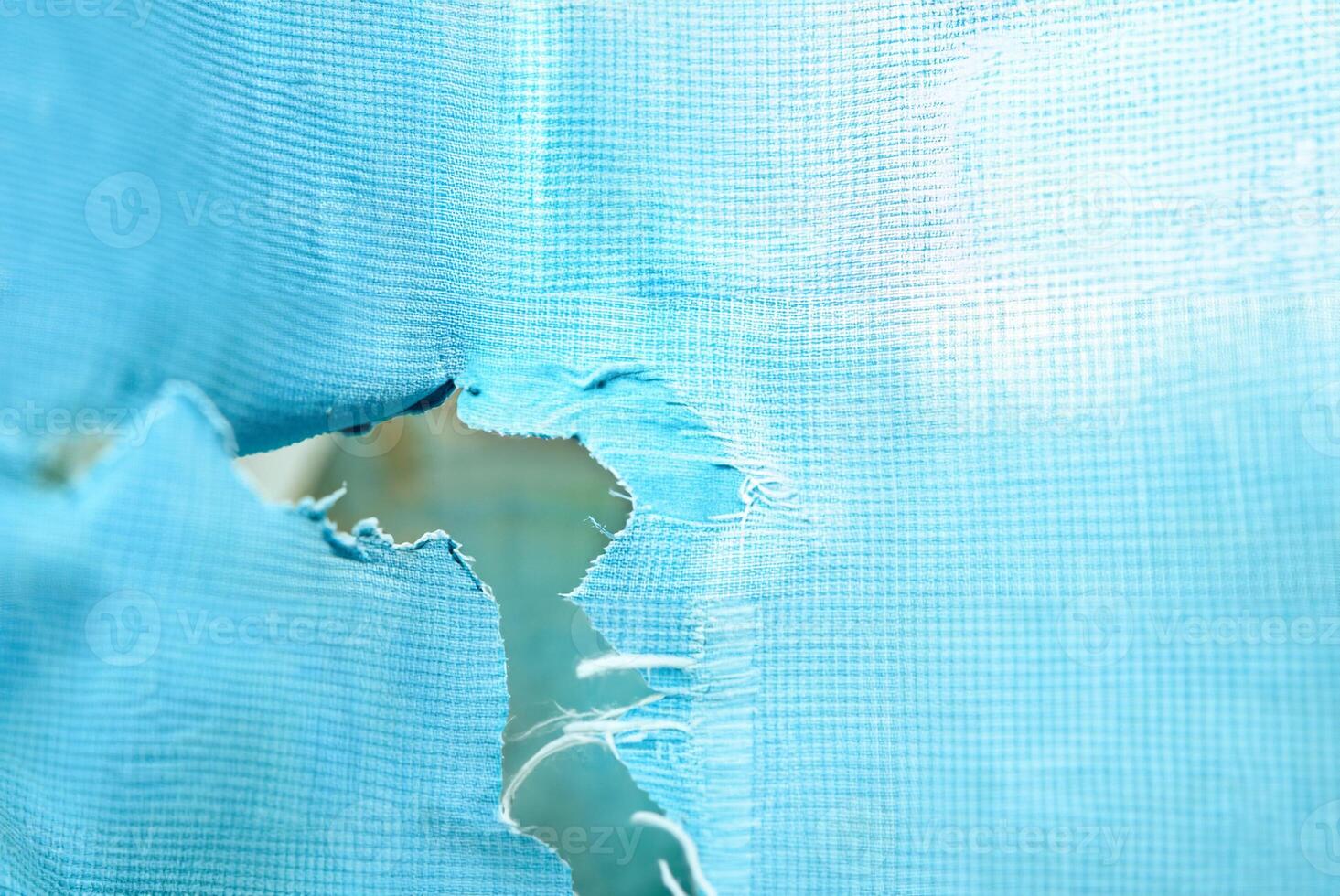 Close-up of a torn blue fabric with a rip in the center, showing visible texture and wear, ideal for concepts of damage or imperfection. photo