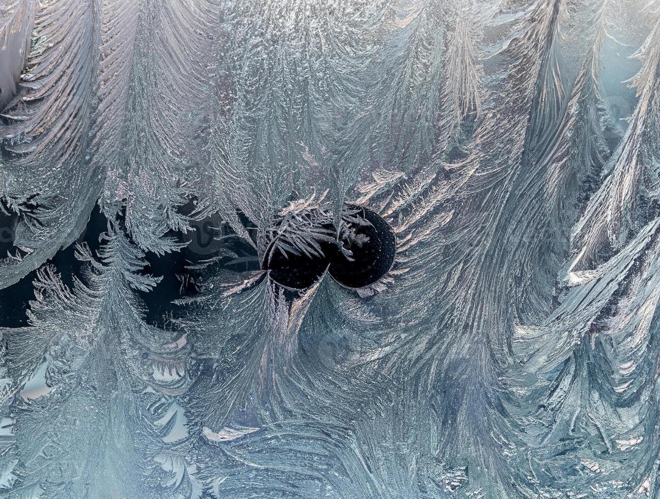 Close-up of intricate ice frost patterns on a glass window, creating a natural, cold, and textured winter background. photo