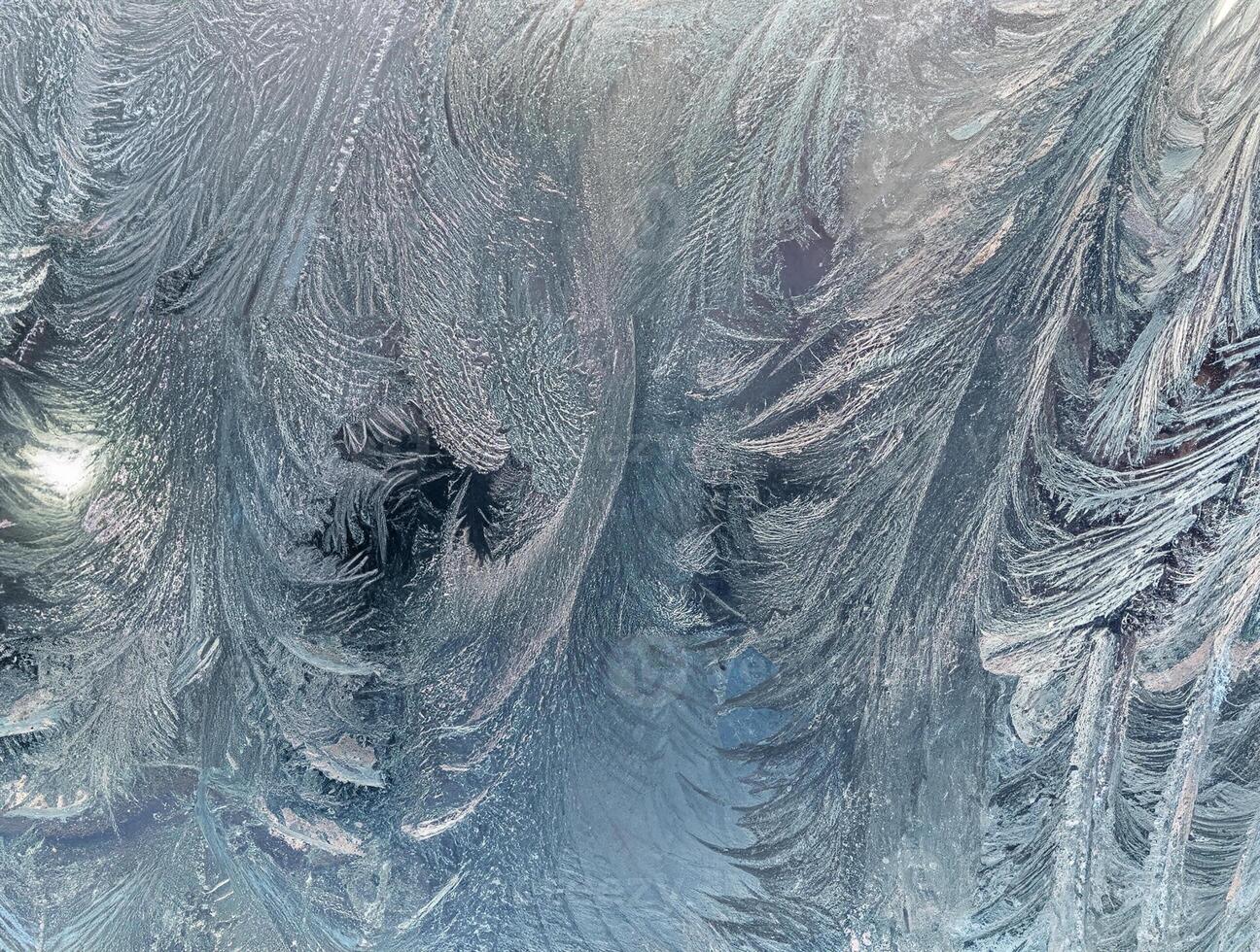 Close-up of intricate ice frost patterns on a glass window, creating a natural, cold, and textured winter background. photo