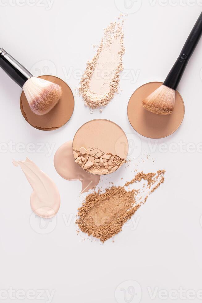 A beautiful cosmetic background with various types of compact powder, strokes of liquid powder, chic brushes for applying makeup. Vertical top view. photo