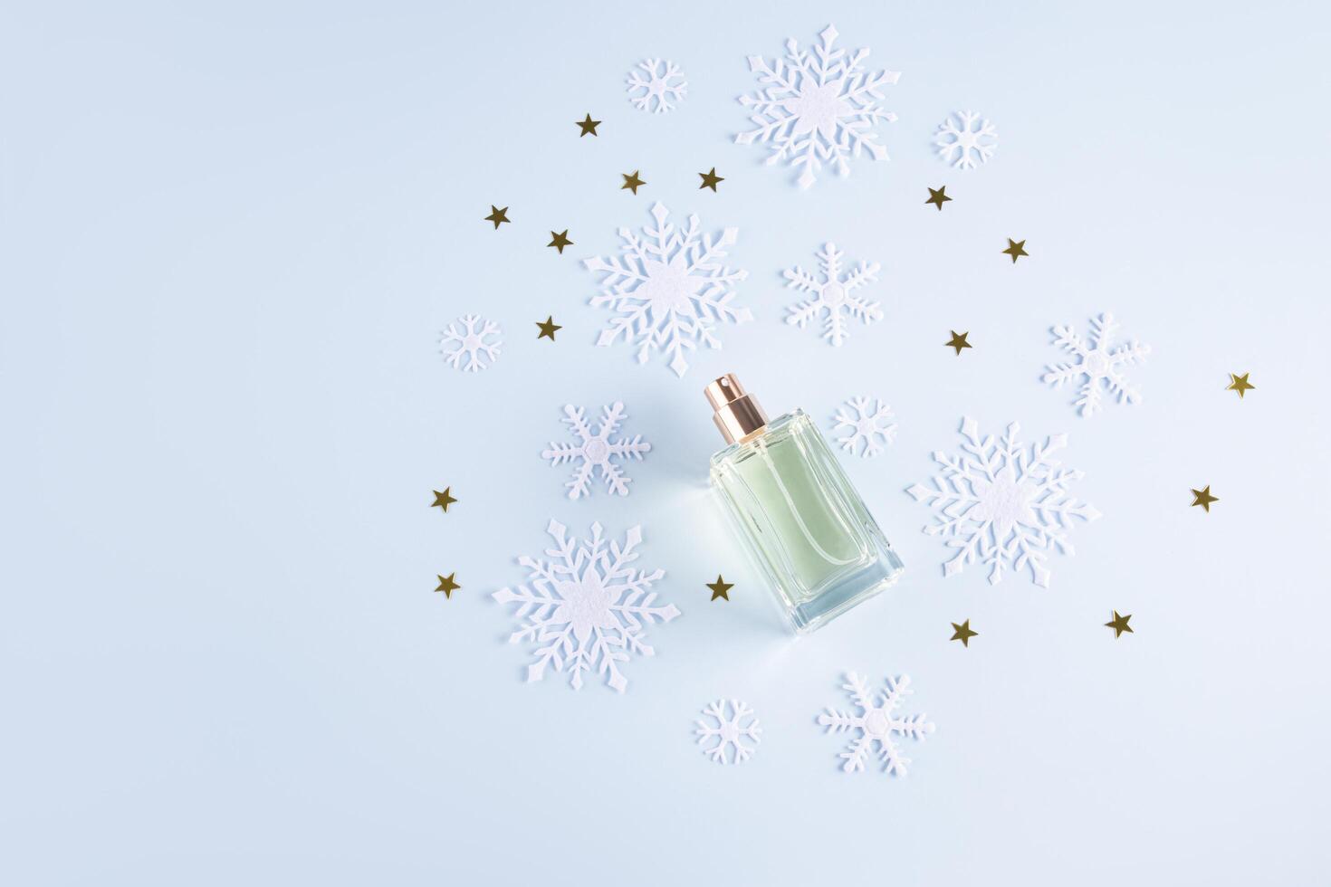 An elegant glass bottle of a cosmetic product or perfume on a light background with golden stars and snowflakes. top view. A blank bottle mockup. photo