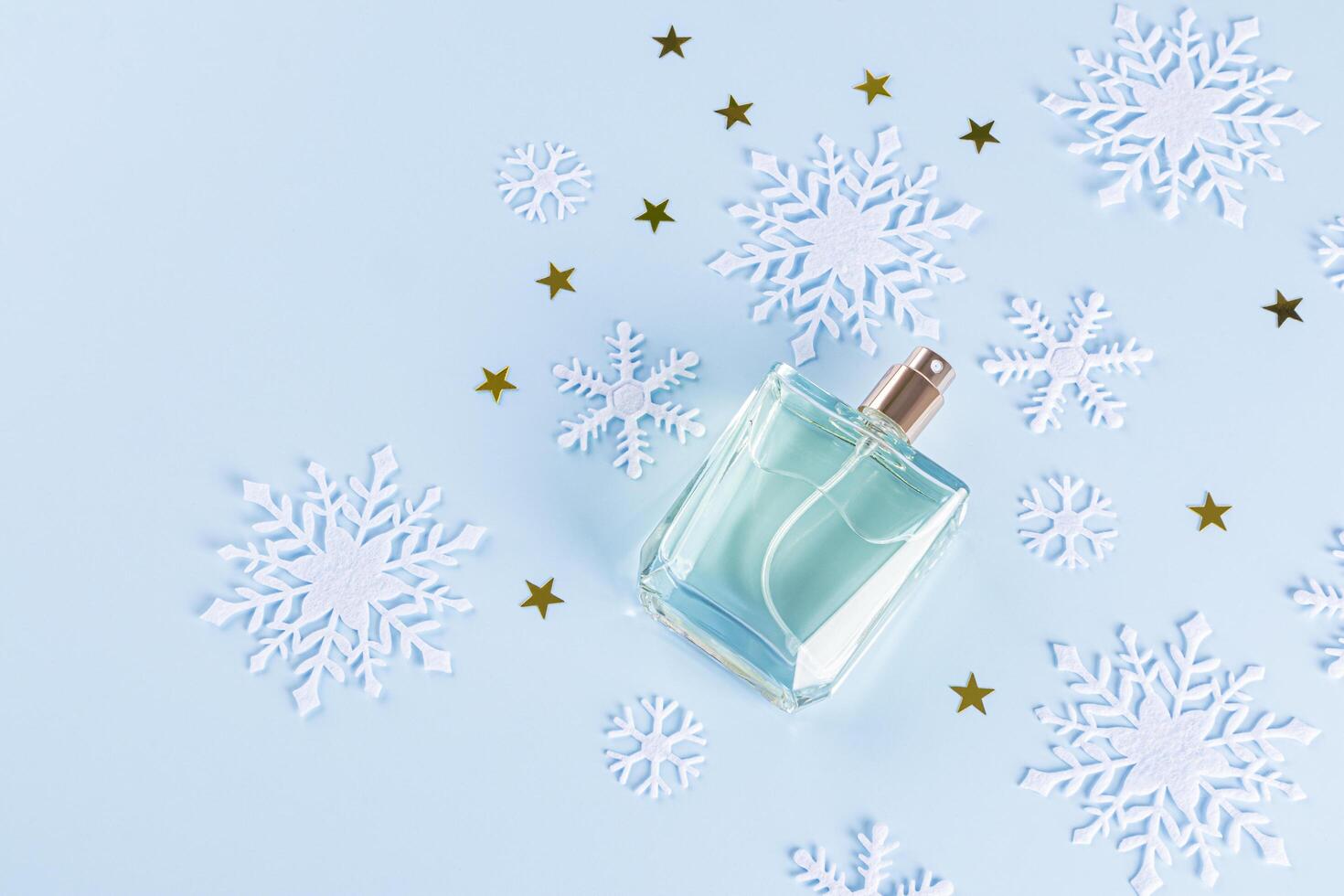 An unbranded perfume bottle on a blue background among decorative snowflakes and golden stars. top view. A copy space. blank bottle mockup. template photo