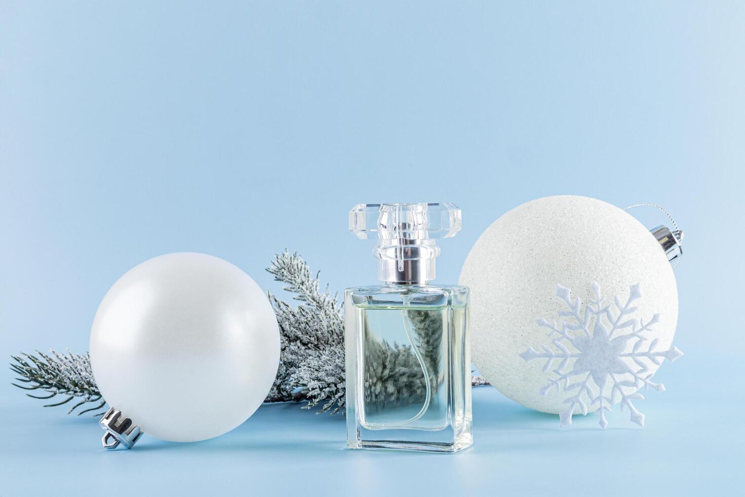A beautiful bottle of perfume against the background of a snow-covered spruce branch and white Christmas balls. Front view. Product presentation photo