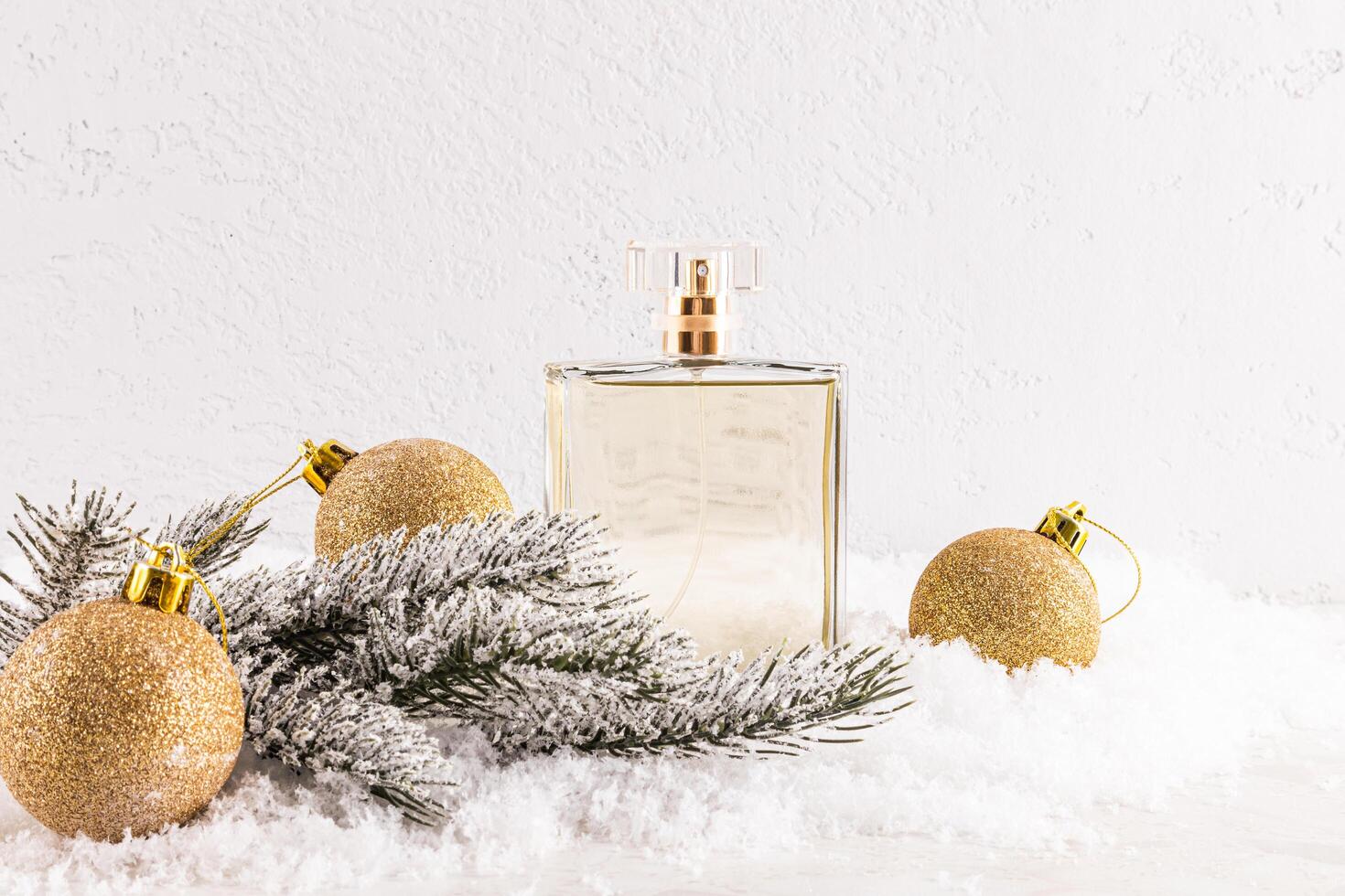A chic bottle of expensive perfume among golden Christmas balls on fluffy snow, a spruce branch. A blank bottle mockup. Front view. white background photo