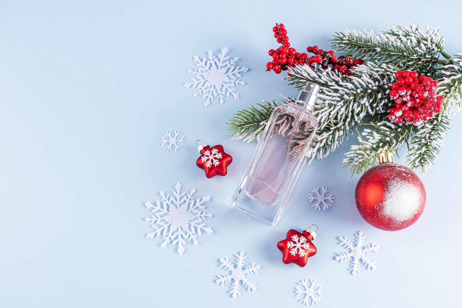 An elegant bottle of women's perfume on a blue background with snowflakes, a spruce branch, red balls. New Year's perfume. A copy space. layout. photo