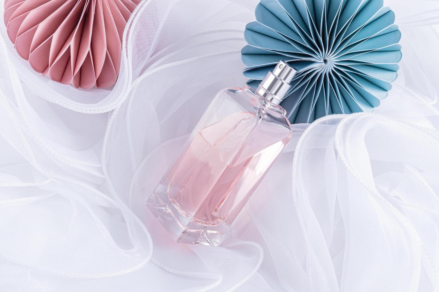 A slim bottle of cosmetic spray or perfume on a white wavy background of silk fabric with New Year's paper toys. top view. The concept of a holiday photo
