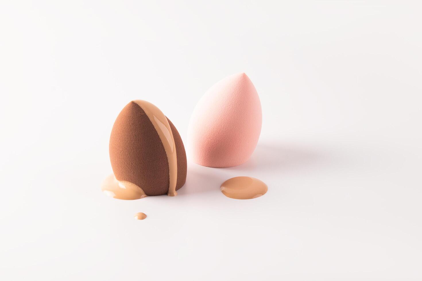 The delicate liquid texture of foundation powder in a natural tone flows down on a blender sponge. Two sponges of different colors. white background photo