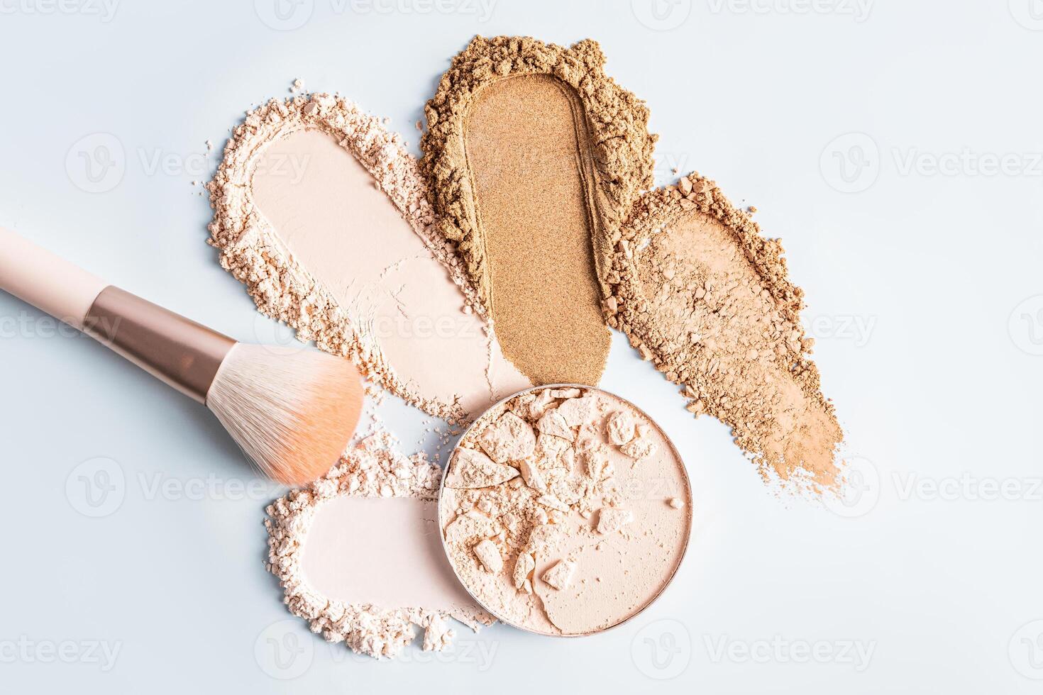 A round block of compact powder with broken pieces, a sample of loose powder of a natural, brown tone with a makeup brush. Blue background. photo