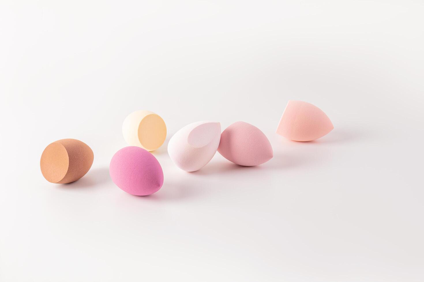 Several beautiful cosmetic sponges blender in the shape of an egg are scattered on a white background . A copy space. Care and beauty concept. photo