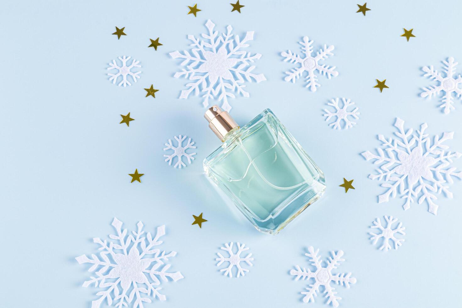 An unbranded perfume bottle on a blue background among decorative snowflakes and golden stars. top view. A copy space. blank bottle mockup. template photo