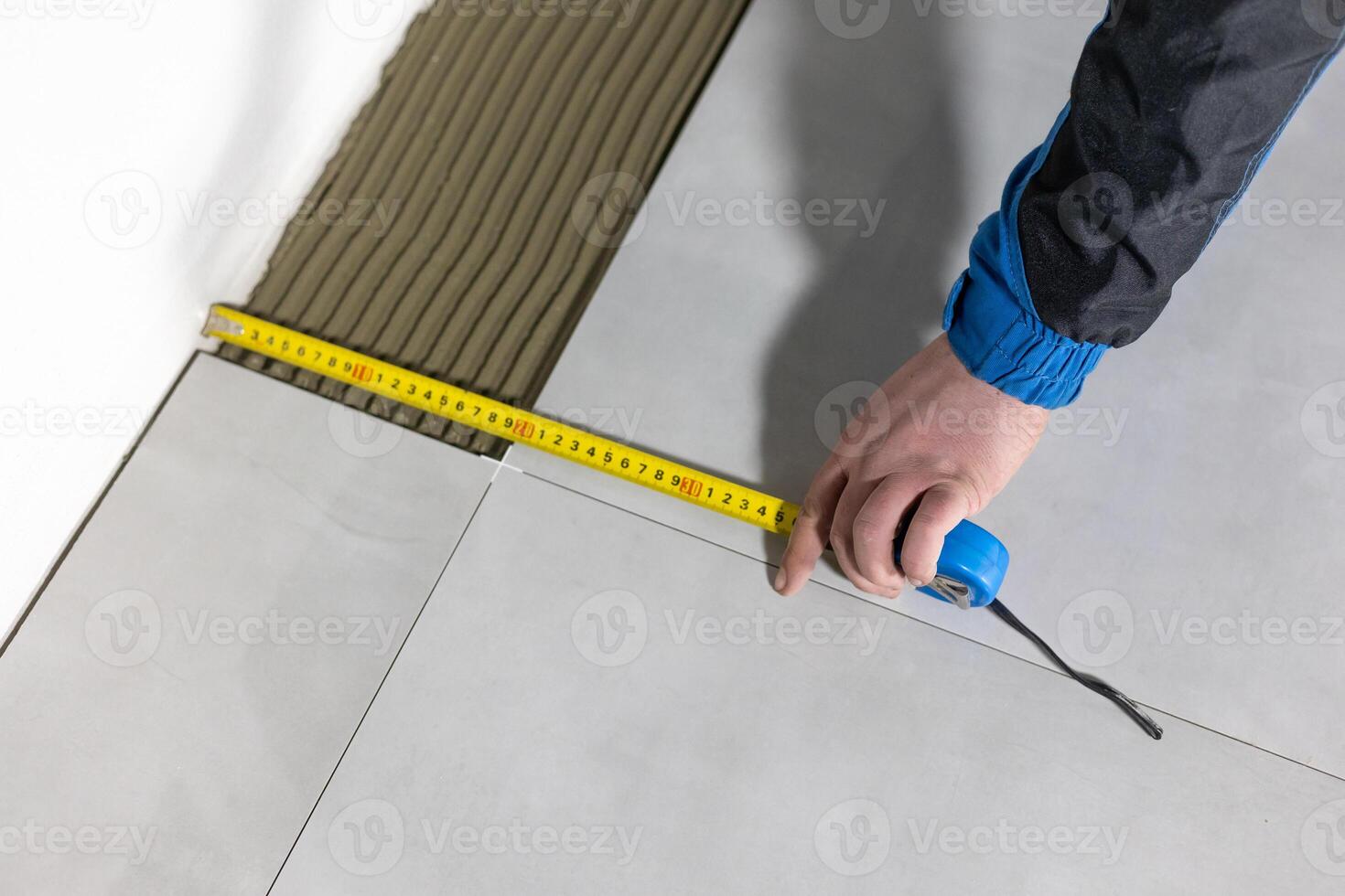 Tiler worker placing or tiling gray ceramic tile in the position over adhesive glue with lash tile leveling system, renovation or recontruction, concept of building photo