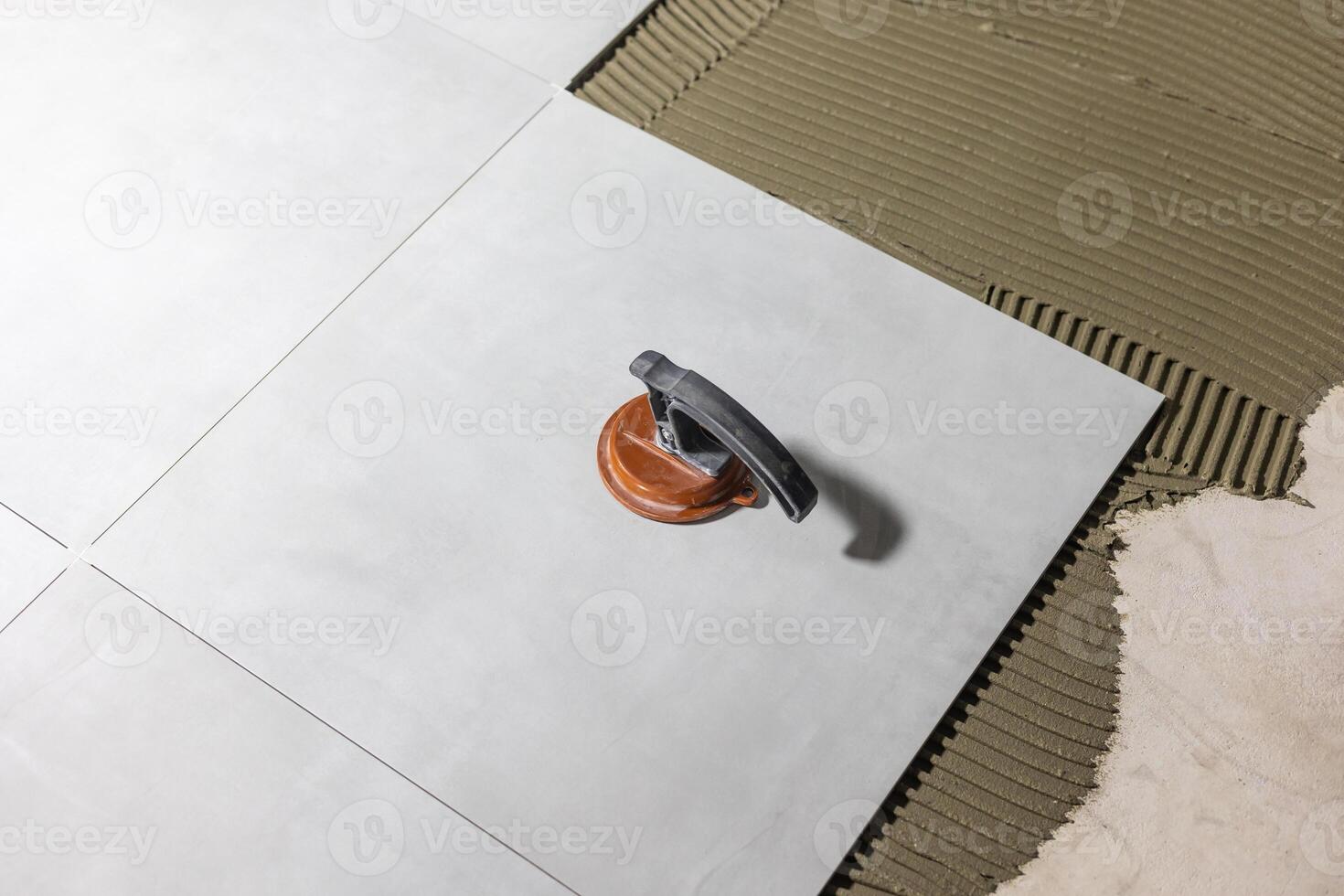 Tiler worker placing or tiling gray ceramic tile in the position over adhesive glue with lash tile leveling system, renovation or recontruction, concept of building photo