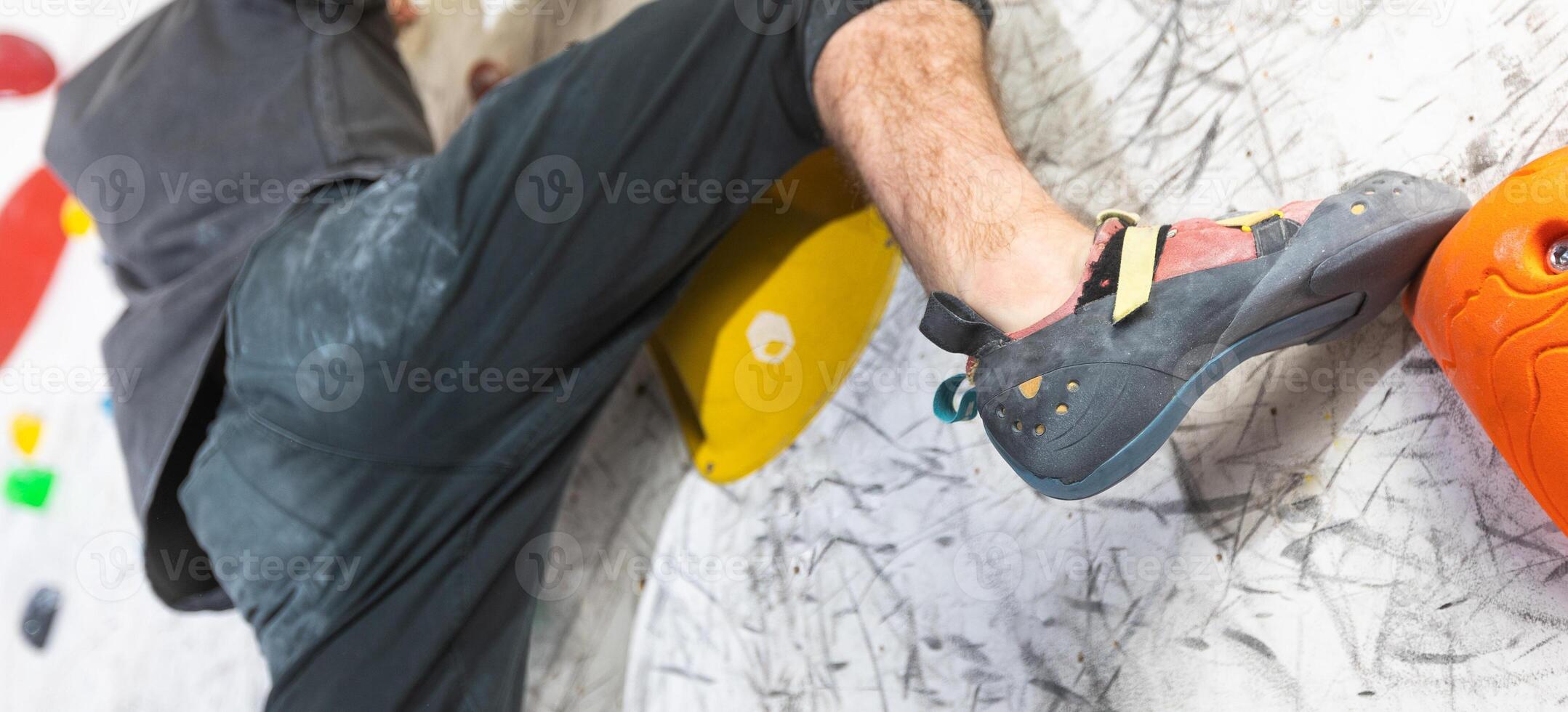 Close up view of young man or climber feet in climbing shoes on artificial indoor wall at climbing center, sport activity concept photo